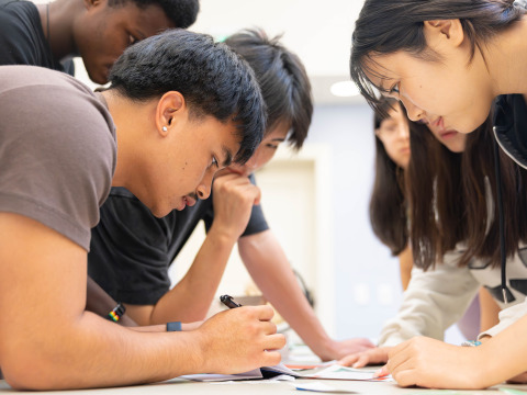 Male and female students lean in and look at items on a table during an escape room activity.