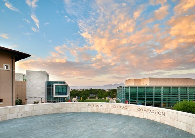 Central values of Soka University, Wisdom, Courage, and Compassion displayed on a wall in front of clouds and silhouetted mountains in the background