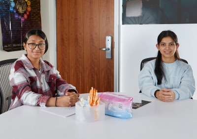 Two women smile at the camera as they sit at a table with menstrual products