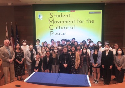 Students and Faculty pose in front of a projected screen that reads "Student Movement for the Culture of Peace"