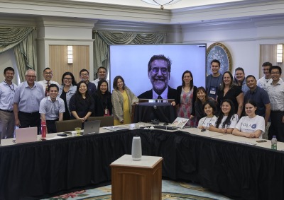 Members of SIGS pose for a photo in front of a tv screen featuring Andrea Bartoli, Executive Adviser of SIGS
