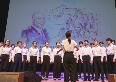 SUA student chorus signs the Light of Hope in front of drawing of Daisaku Ikeda 