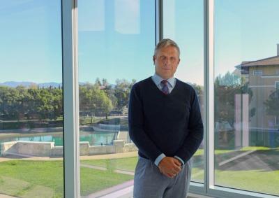 Dean Hamersley poses in front of glass windows on Soka University of America's campus