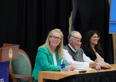 Three panelists sit at a desk together during the SBS Symposium