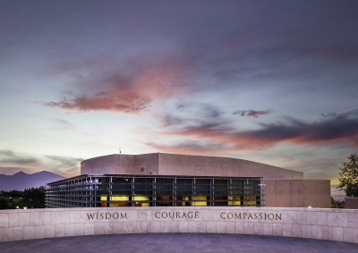 An overlook on SUA's campus displays the words "Wisdom, Courage, Compassion" in front of the Performing Arts Center which is lit up during dusk.