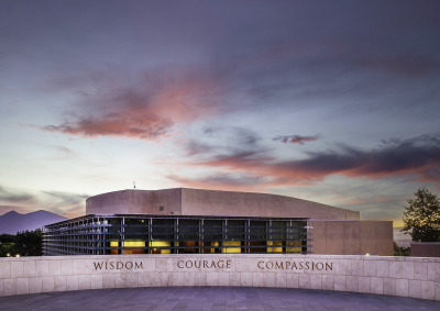 An overlook on SUA's campus displays the words "Wisdom, Courage, Compassion" in front of the Performing Arts Center which is lit up during dusk.