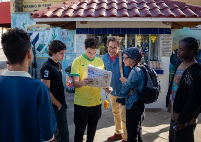 Six people stand together and look intently at a newspaper during a photo walk in Little Havana, Miami.