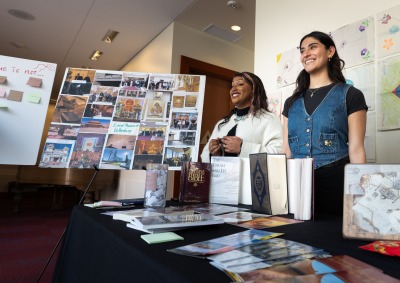 Two students smile as they stand with their research project during the winter block Learning Cluster Fair.