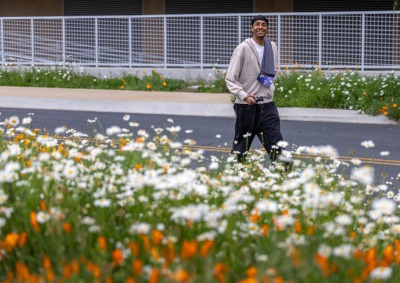 Lucas Colombo ’27 smiles at the camera as he walks among flowers on SUA's campus during the annual Heart of a Lion walk/run.