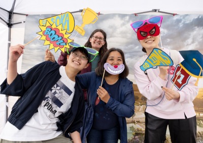 Four people pose with props in front of an SUA campus backdrop during the 2025 Soka Homecoming event.