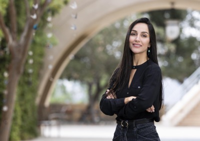 Foroogh Farhang crosses her arms and smiles at the camera outside on SUA's campus.