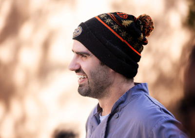 Side profile shot of a bearded man wearing a grey chef shirt and a black Anaheim Ducks holiday beanie smiles.