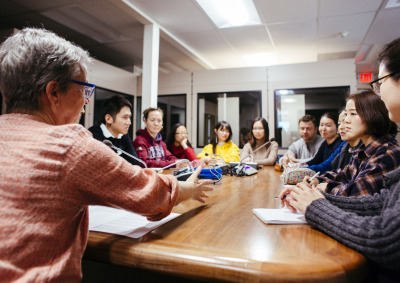A group of 11 people sit around an oval wooden table and take part in a discussion.