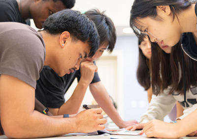 Male and female students lean in and look at items on a table during an escape room activity.