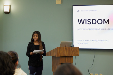 A speaker stands beside the podium as she presents during a seminar series