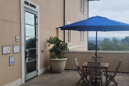 Exterior of Mail Center with mail slots, posted hours, and a picnic table with blue umbrella outside the entrance.