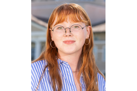 Tess Aman wears glasses and a blue shirt in a headshot
