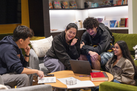 Four students laugh as they work on coursework together.