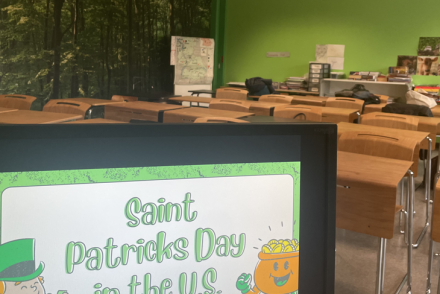 A sign reading "Saint Patricks Day in the US" is displayed at the entrance of a classroom with desks