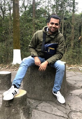 Student in jeans and a green jacket smiling at camera
