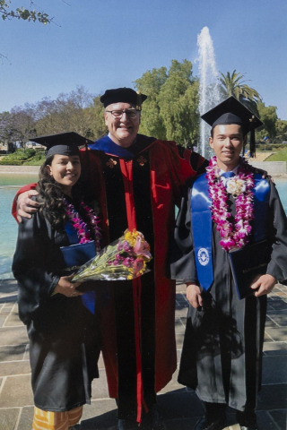 A professor standing between two students on commencement ceremony
